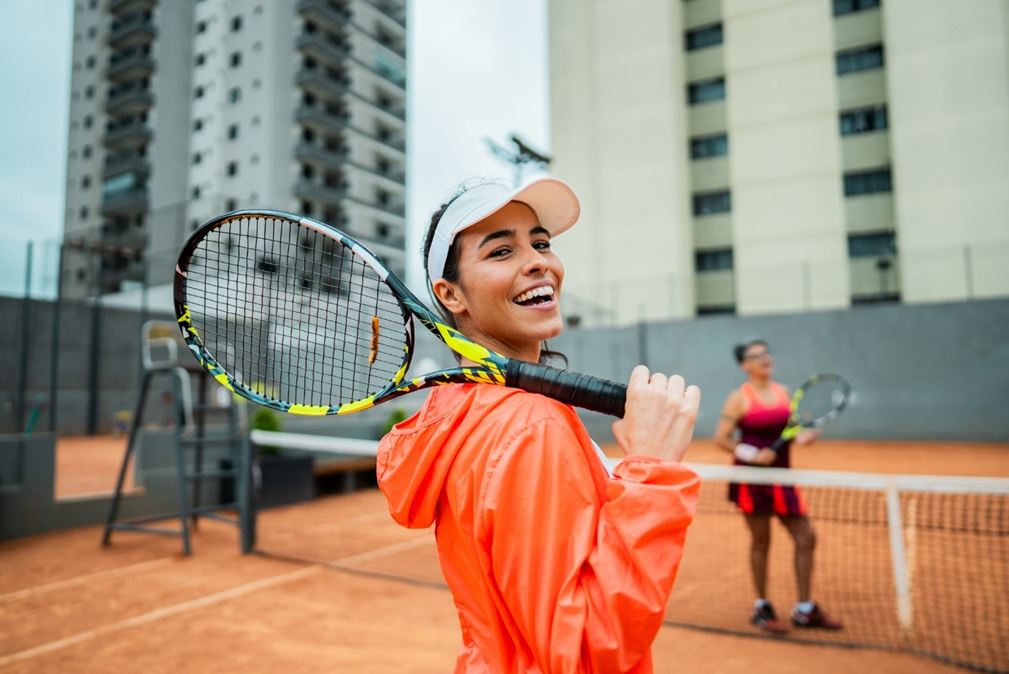 A smiling woman holding a tennis racquet representing tennis elbow prevention in spring sports activities.